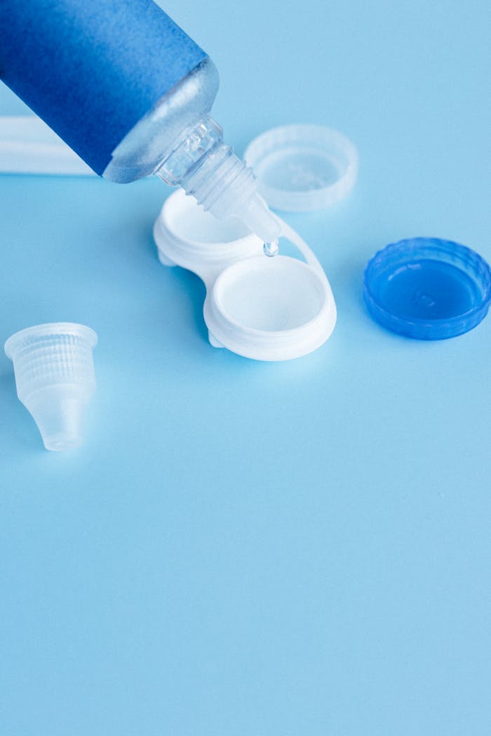 Contact lens solution pouring into a white contact lens case on a blue background.