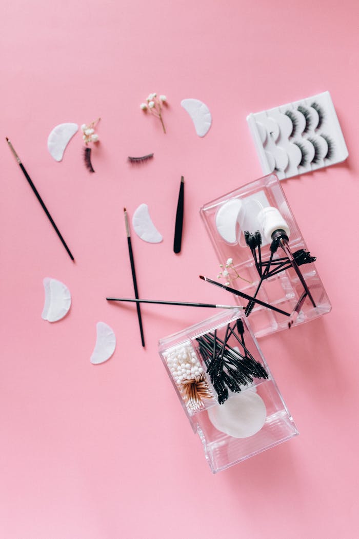 Flat lay of makeup tools and accessories on a pink background, ideal for beauty projects.